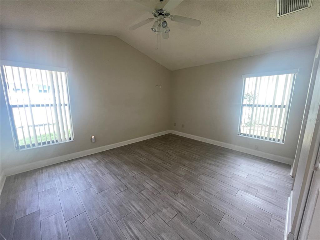 An empty room features light gray wood-look tile flooring, vaulted ceilings, and two windows — 13104 BARTH PLACE UNIT 13104, RIVERVIEW, FL