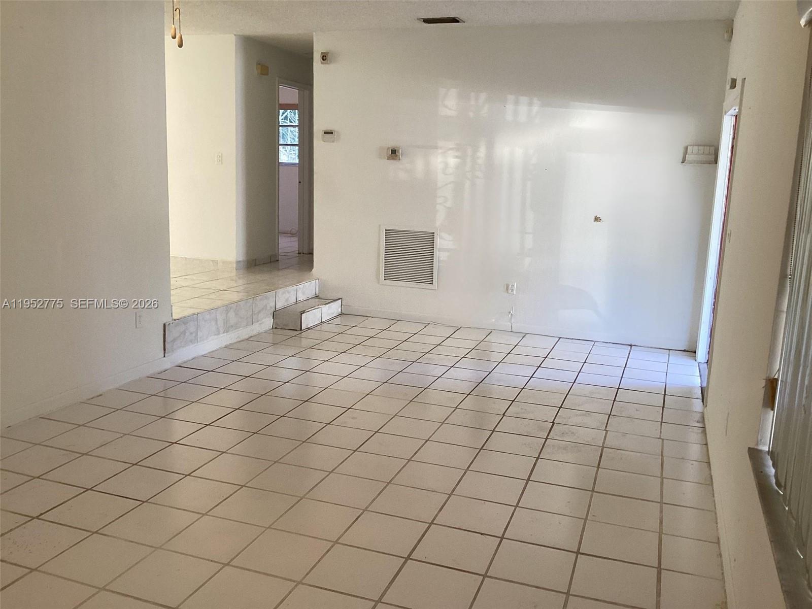 An empty room features white tiled floors, a raised platform area, and white walls — 4824 NW 15th Ct, Miami FL 33142, MIAMI, FL
