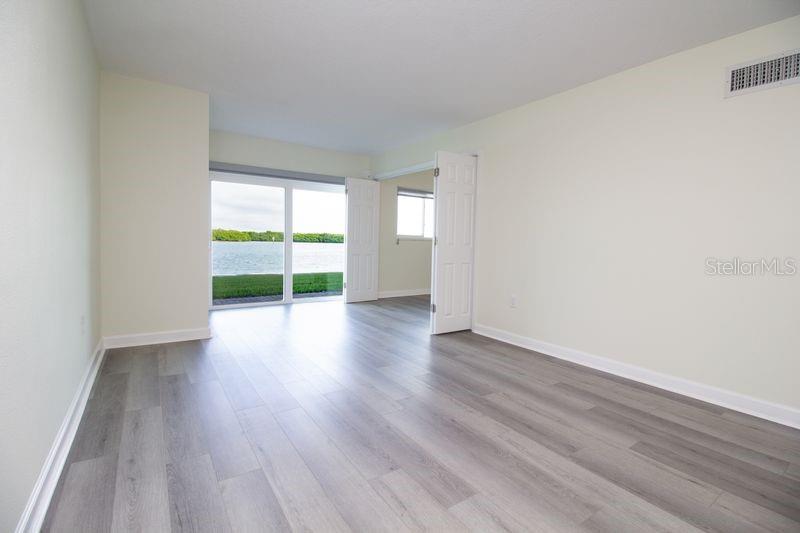 An empty room with light wood-look flooring and double doors opening to a water view — 280 126TH AVENUE UNIT 108, TREASURE ISLAND, FL