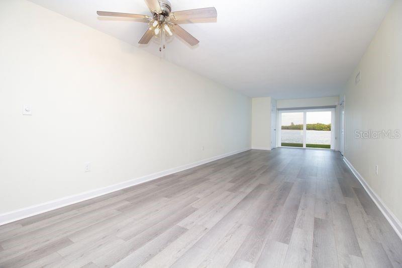 An empty living room with light wood-look flooring, a ceiling fan, and a water view — 280 126TH AVENUE UNIT 108, TREASURE ISLAND, FL