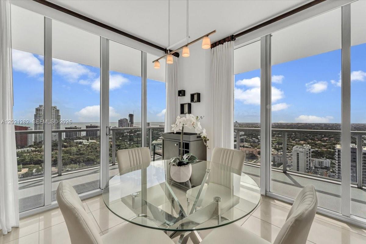 A dining area with a glass table and chairs overlooks a city skyline through windows — 79 SW 12th St, Miami FL 33130, MIAMI, FL