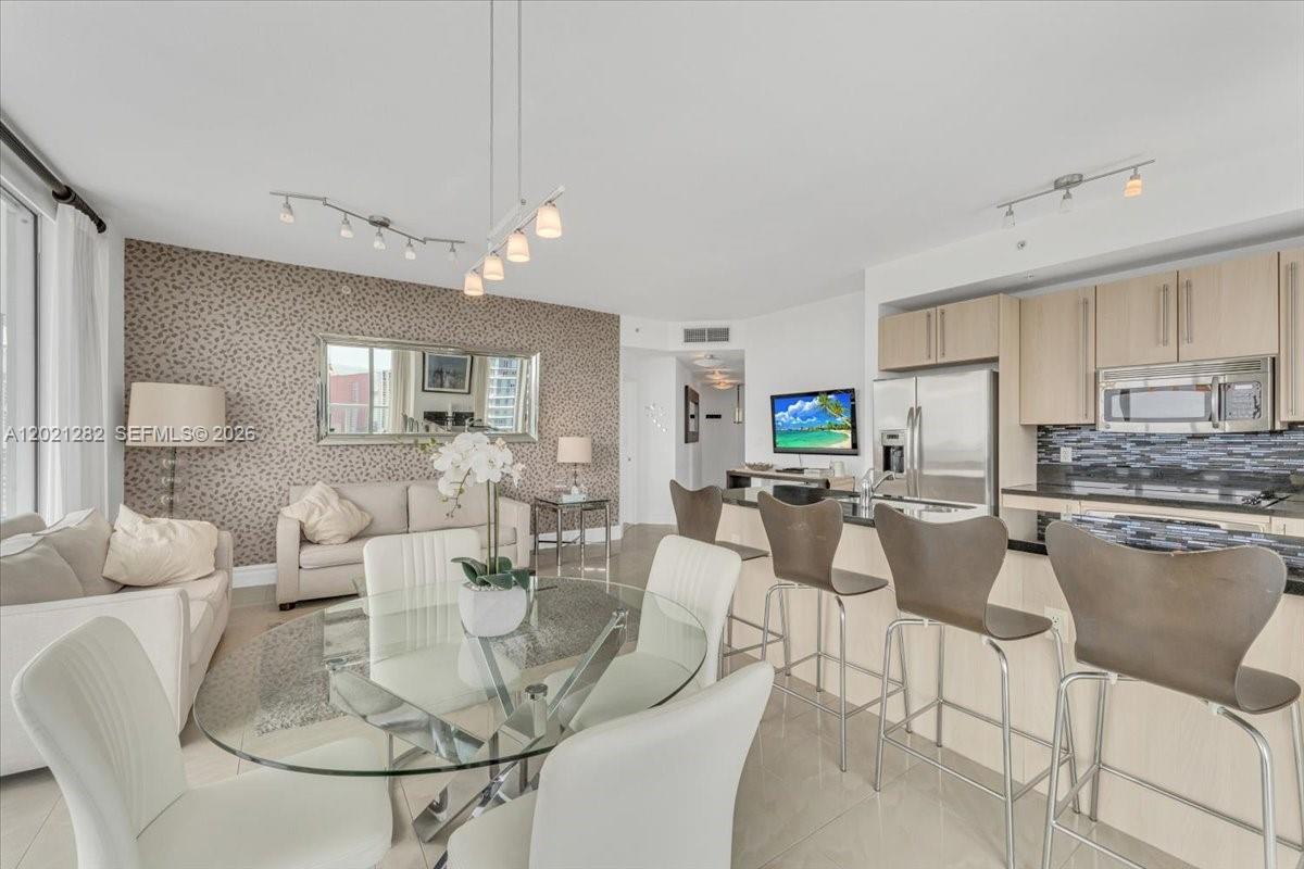 An open-concept living and dining area features a modern kitchen, glass table, and patterned wallpaper — 79 SW 12th St, Miami FL 33130, MIAMI, FL