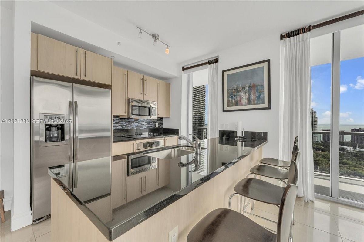 A modern kitchen features light wood cabinets, black countertops, stainless steel appliances, and balcony views — 79 SW 12th St, Miami FL 33130, MIAMI, FL