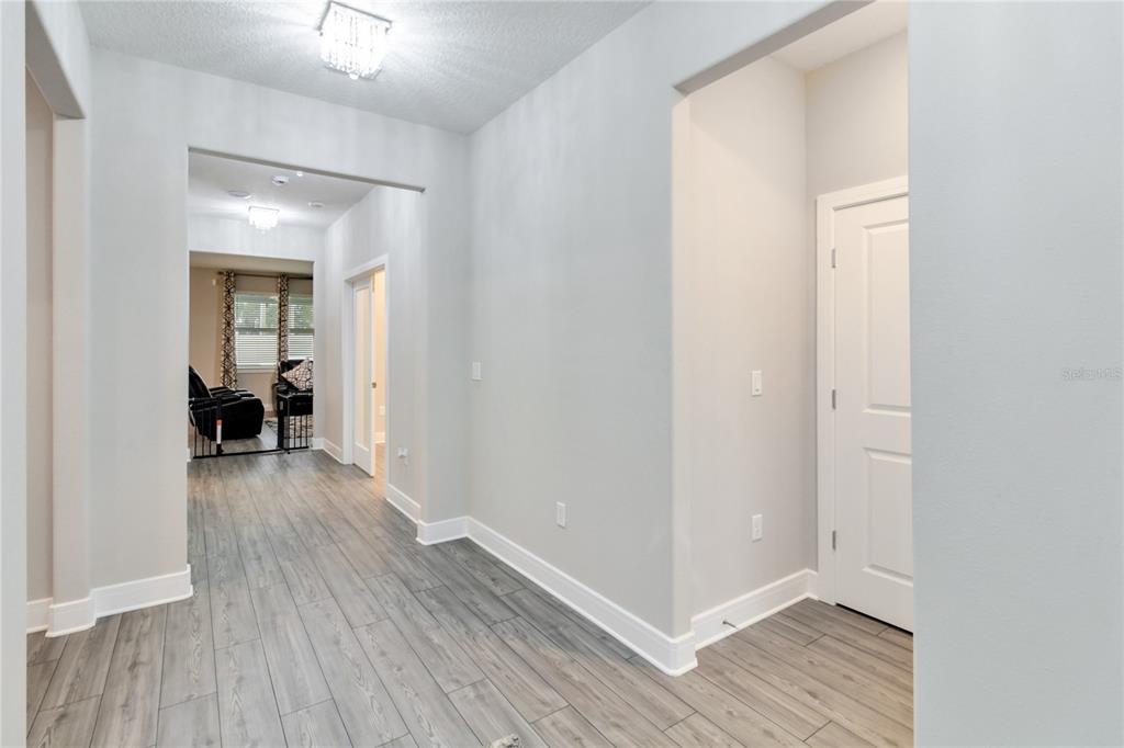 A hallway with light gray walls, wood-look tile flooring, and white trim leads to a room — 4067 MEANDERING BAY DRIVE, APOPKA, FL