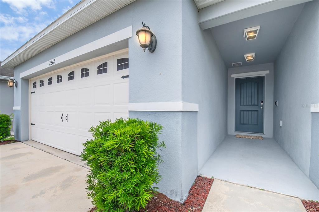 A light blue house exterior features a white garage door, a front porch, and landscaping — 2865 MOSSHIRE CIRCLE, ST CLOUD, FL