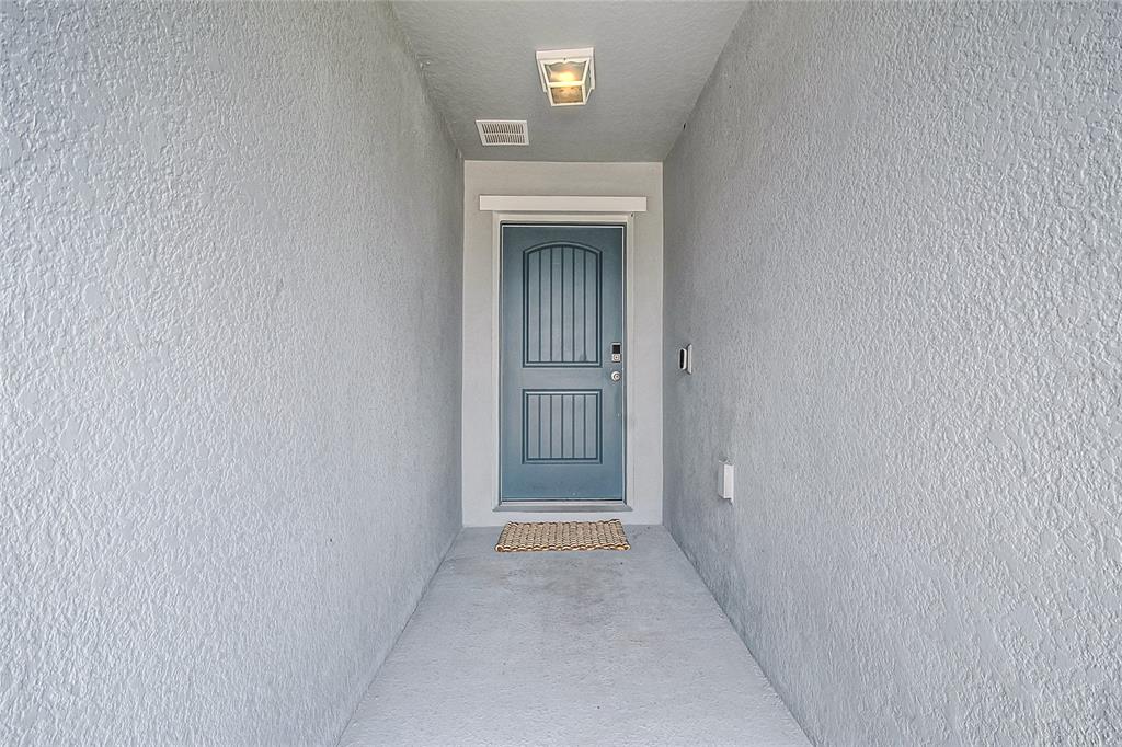 A covered entryway features a blue front door, a light fixture, and a textured wall — 2865 MOSSHIRE CIRCLE, ST CLOUD, FL