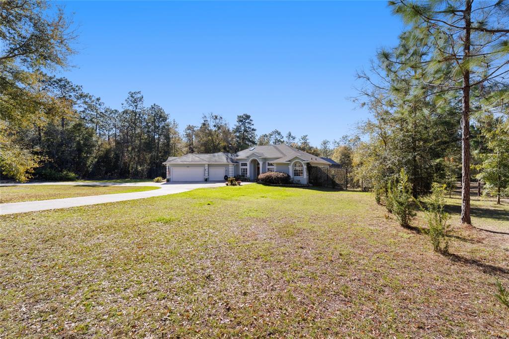 A single-story house with a two-car garage sits on a large, grassy, wooded lot — 12880 SW 66TH STREET, OCALA, FL