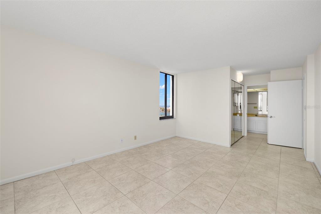An empty bedroom features light-colored tile flooring, white walls, and a window with water views — 9425 BLIND PASS ROAD UNIT 1008, ST PETE BEACH, FL