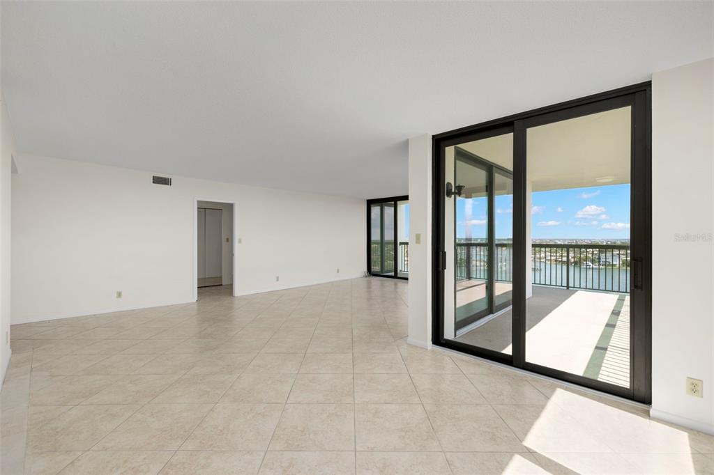 An empty living area with beige tile flooring and sliding glass doors leading to a balcony — 9425 BLIND PASS ROAD UNIT 1008, ST PETE BEACH, FL