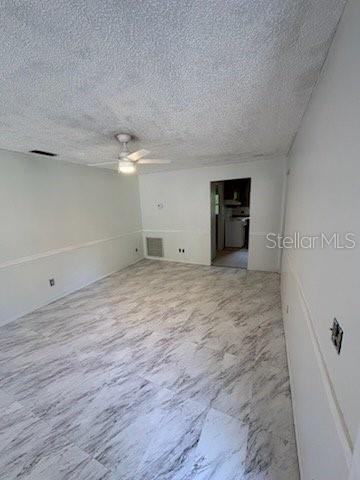 An empty room features white walls, a ceiling fan, and light-colored marble-patterned tile flooring — 2558 N COUNTY RD #470, LAKE PANASOFFKEE, FL