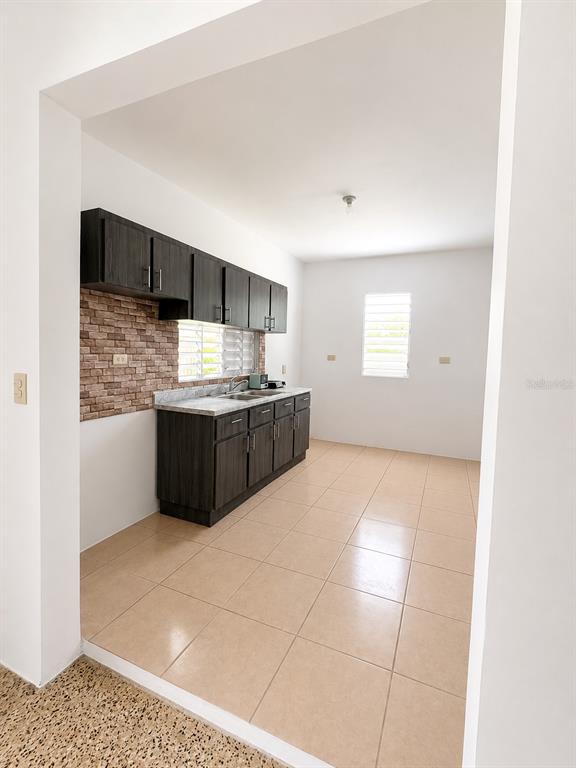A kitchen features dark wood cabinets, a brick-patterned backsplash, and light-colored floor tiles — 11 SINGAPUR, JUANA DIAZ, PR
