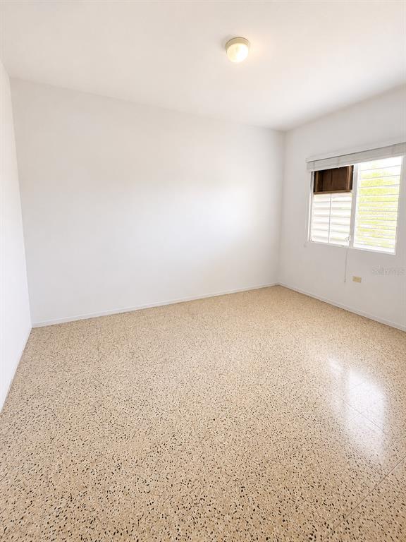 An empty room features white walls, a light-colored speckled tile floor, and a single window — 11 SINGAPUR, JUANA DIAZ, PR