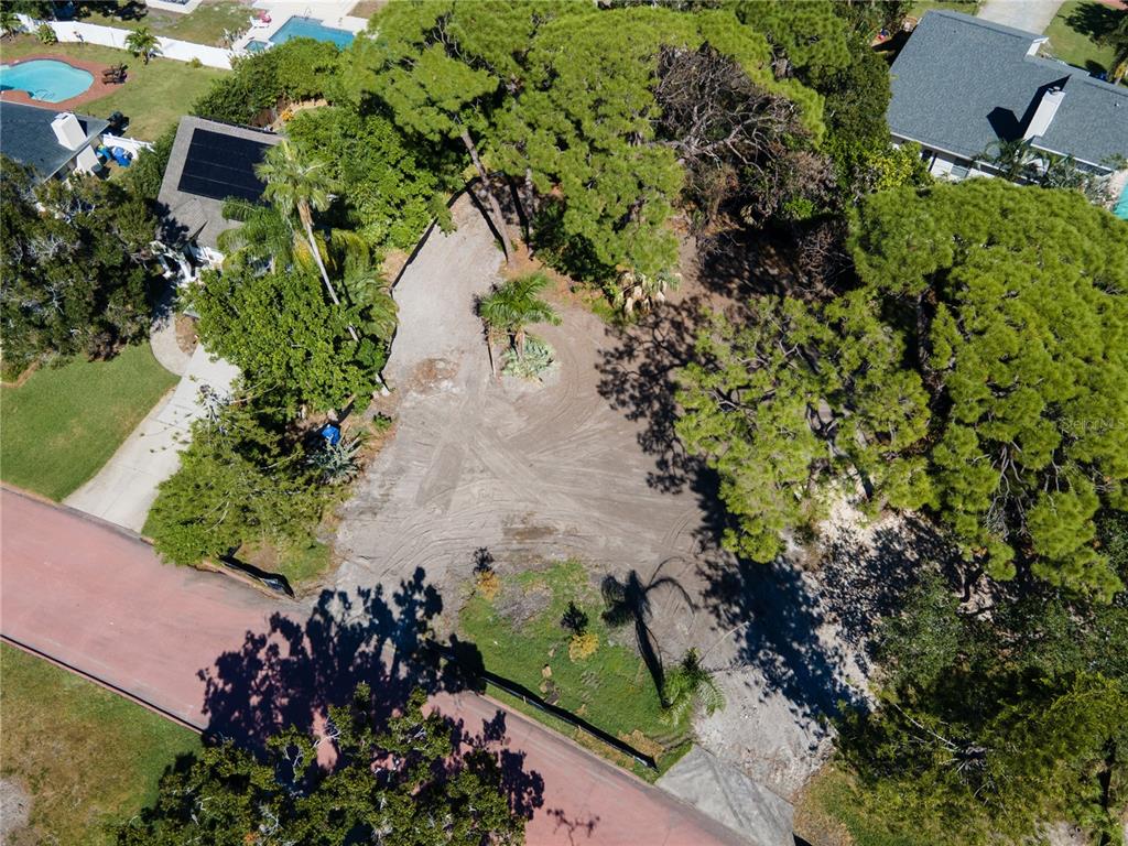 An aerial view shows a cleared, sandy residential lot surrounded by trees and neighboring houses — 1125L FRIENDLY WAY S, ST PETERSBURG, FL