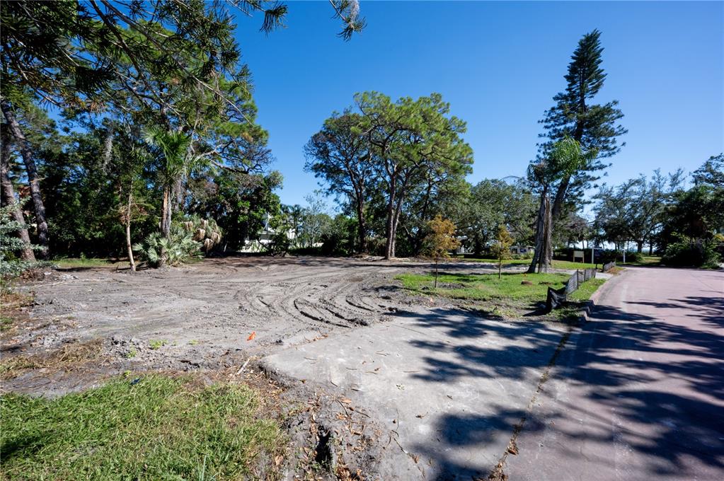 A vacant, cleared residential lot features tire tracks, mature trees, and a concrete driveway apron — 1125L FRIENDLY WAY S, ST PETERSBURG, FL