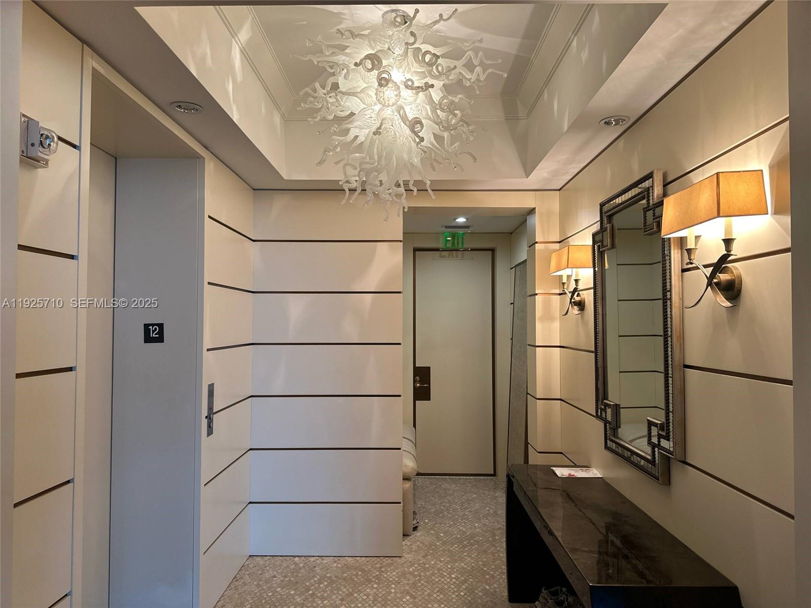 A modern hallway features a white chandelier, wall sconces, a mirror, and a console table — 10295 Collins Ave # 1203, Bal Harbour FL 33154, BAL HARBOUR, FL