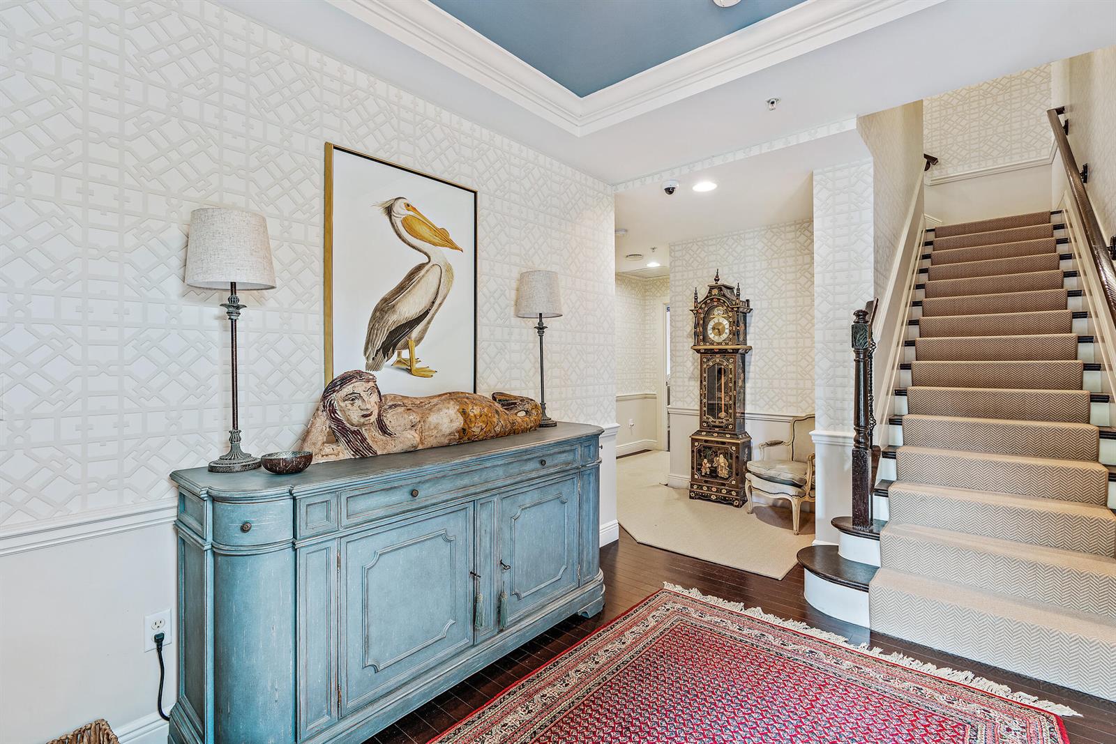 A foyer features a blue sideboard, a pelican painting, a grandfather clock, and a staircase — 126 Tierra Lane # 4, Jupiter FL 33477, JUPITER, FL