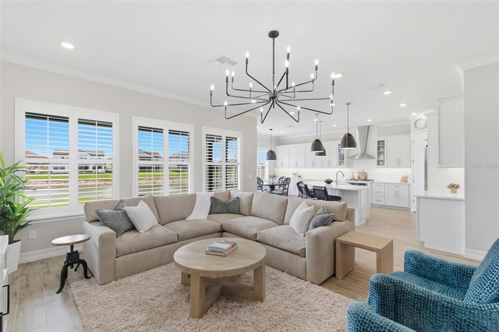 An open-concept living room and kitchen featuring a sectional sofa, chandelier, and white cabinetry — 29657 PICANA LANE, WESLEY CHAPEL, FL