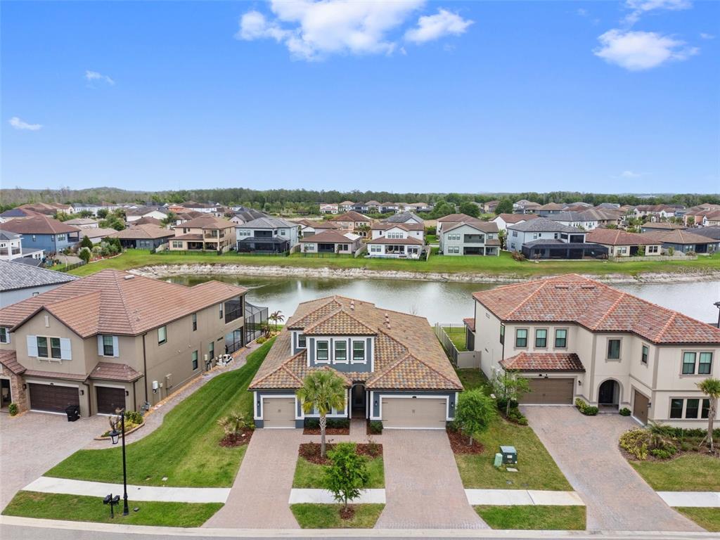 An aerial view shows three suburban houses with tile roofs facing a small lake — 29657 PICANA LANE, WESLEY CHAPEL, FL