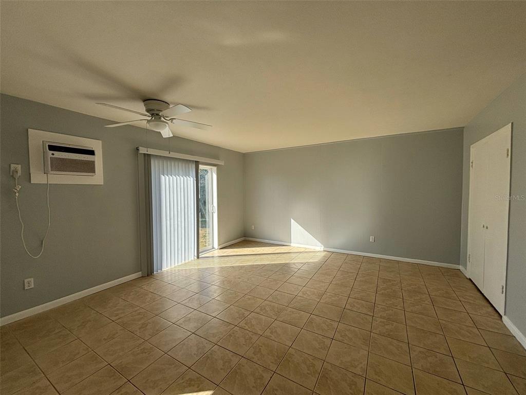 An empty room features light gray walls, beige tile flooring, a ceiling fan, and sliding doors — 310 FARNOL STREET SW UNIT 3, WINTER HAVEN, FL