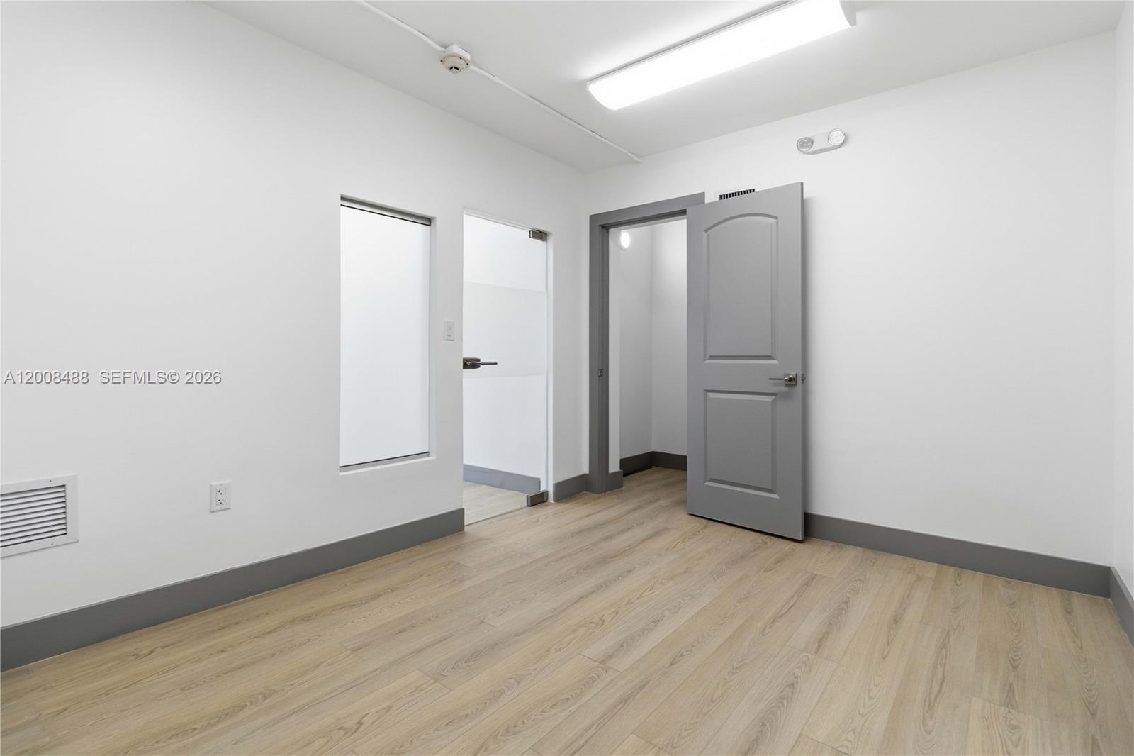An empty room features light wood-look flooring, white walls, gray baseboards, and two doorways — 470 NW 22nd Ave, Miami FL 33125, MIAMI, FL