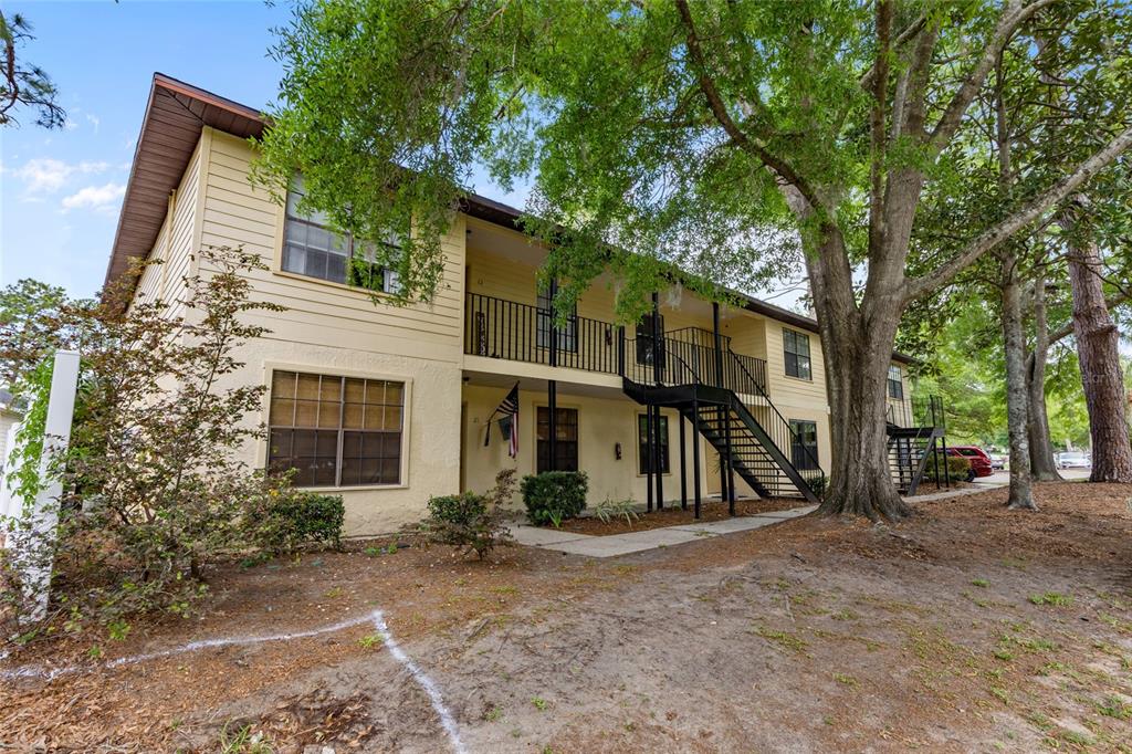 A two-story apartment building with yellow siding, a black metal staircase, and large oak trees — 6400 NW 106TH PLACE UNIT 20, ALACHUA, FL