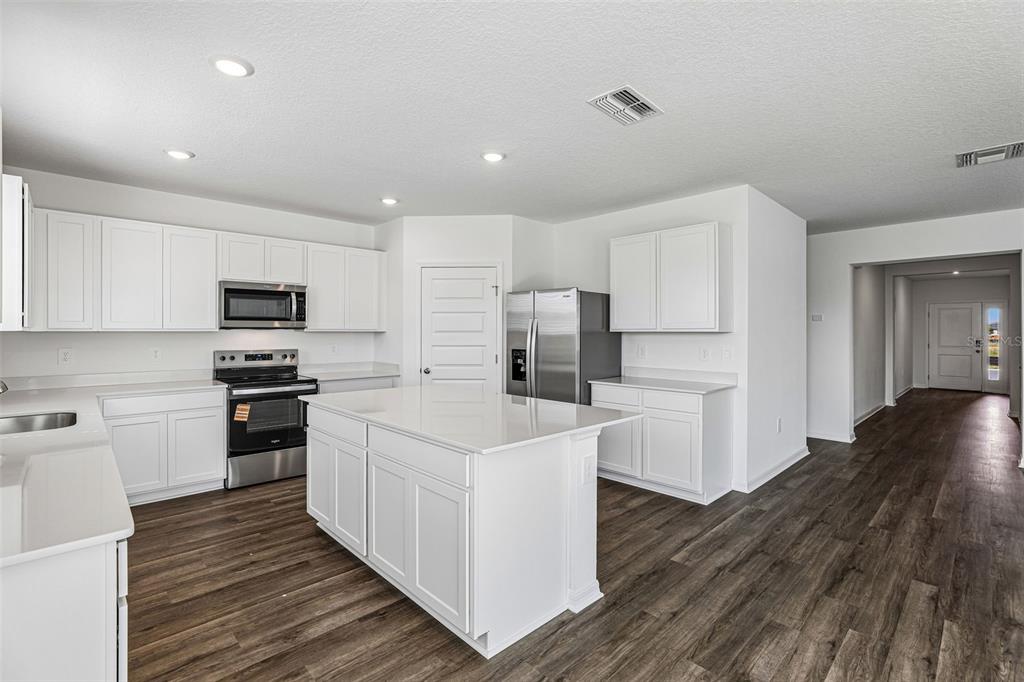 A modern kitchen features white cabinets, stainless steel appliances, a center island, and wood-look flooring — 3914 LIMEKLIN FALLS LOOP, DAVENPORT, FL