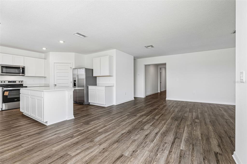 A kitchen with white cabinets and stainless steel appliances opens to a spacious living area — 3914 LIMEKLIN FALLS LOOP, DAVENPORT, FL