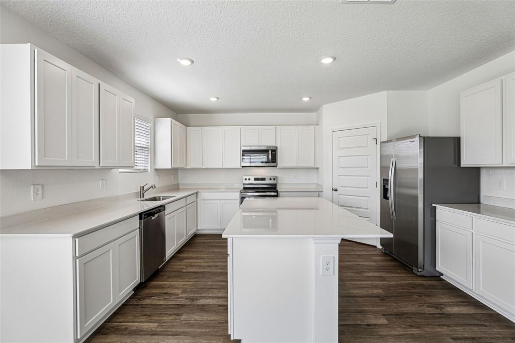 A modern kitchen features white cabinets, stainless steel appliances, a center island, and wood flooring — 3914 LIMEKLIN FALLS LOOP, DAVENPORT, FL