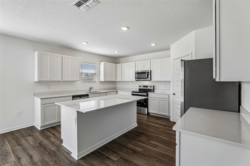 A modern kitchen features white cabinetry, a central island, stainless steel appliances, and wood flooring — 3914 LIMEKLIN FALLS LOOP, DAVENPORT, FL