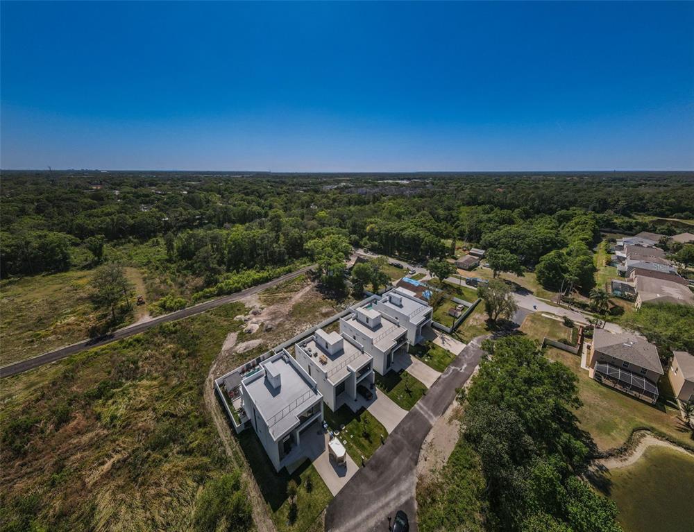 An aerial view shows three modern white townhomes situated next to a wooded area — 210 SKYTRAIL, TAMPA, FL