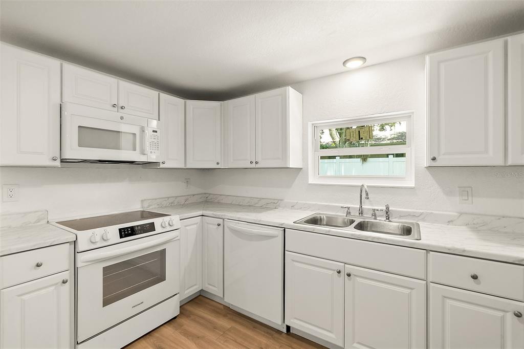 A kitchen features white cabinets, white appliances, and marble-patterned countertops — 607 WAYNE AVENUE, NEW SMYRNA BEACH, FL