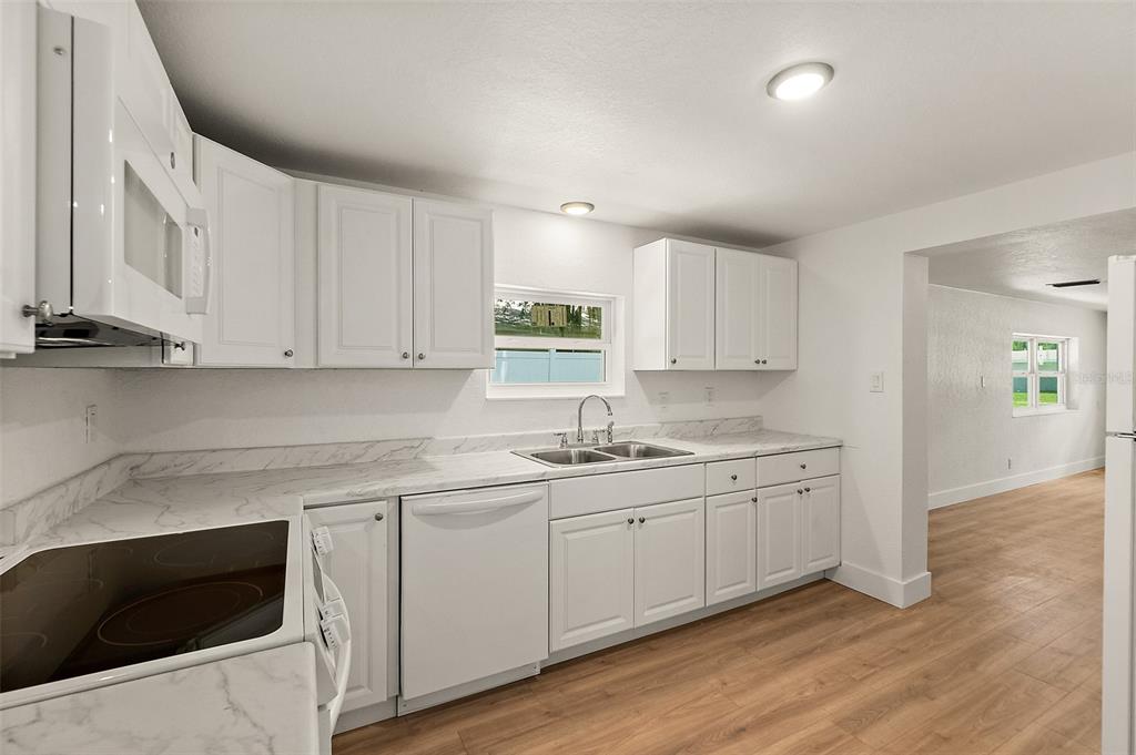 A kitchen with white cabinets, marble-look countertops, stainless steel sink, and light wood flooring — 607 WAYNE AVENUE, NEW SMYRNA BEACH, FL