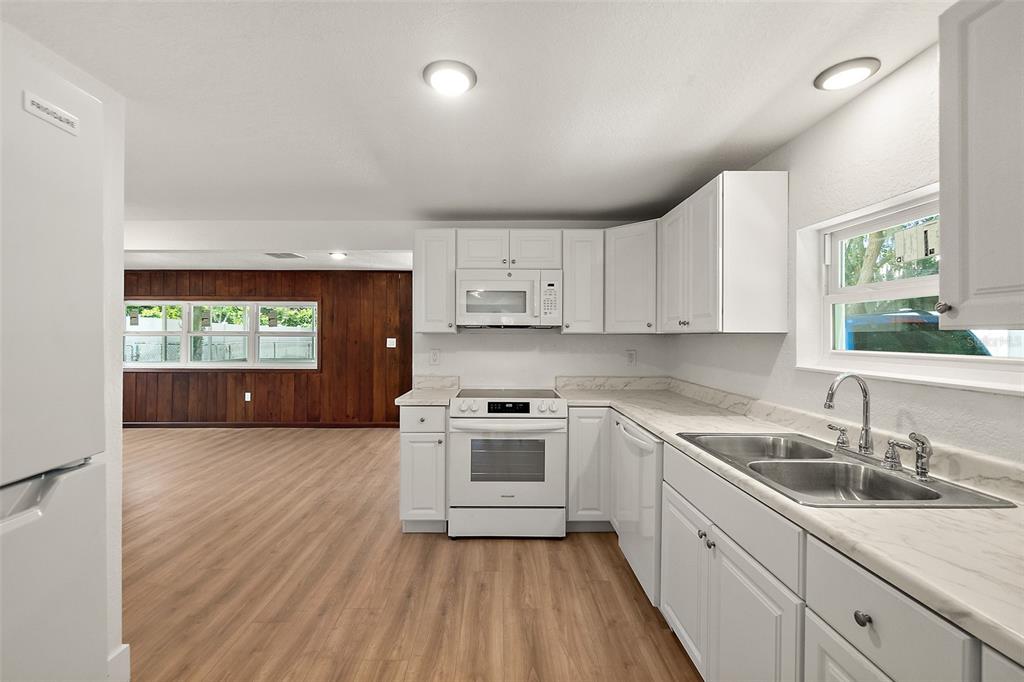 A white kitchen with wood-look flooring opens to a living area with wood-paneled walls — 607 WAYNE AVENUE, NEW SMYRNA BEACH, FL