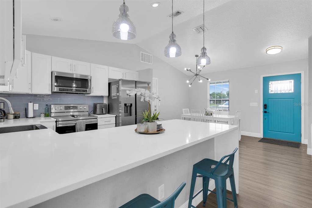 A modern kitchen features white cabinets, a large quartz island, and a bright blue door — 8115 WINDY HILL WAY, ORLANDO, FL