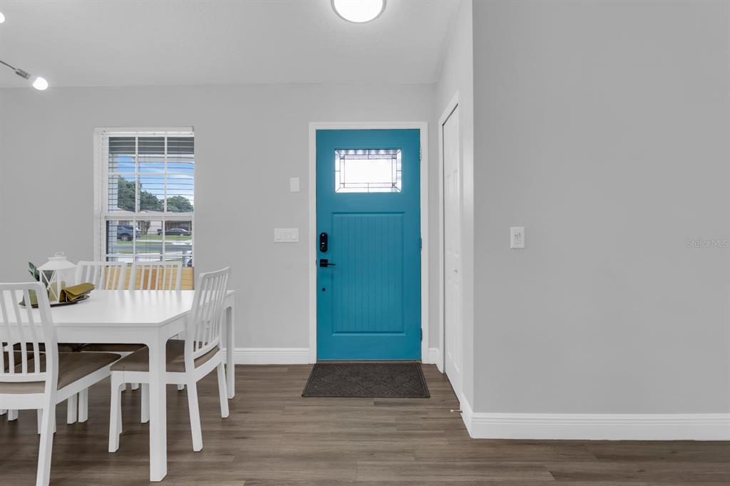 A dining area features a white table, white chairs, wood-look flooring, and a bright blue door — 8115 WINDY HILL WAY, ORLANDO, FL