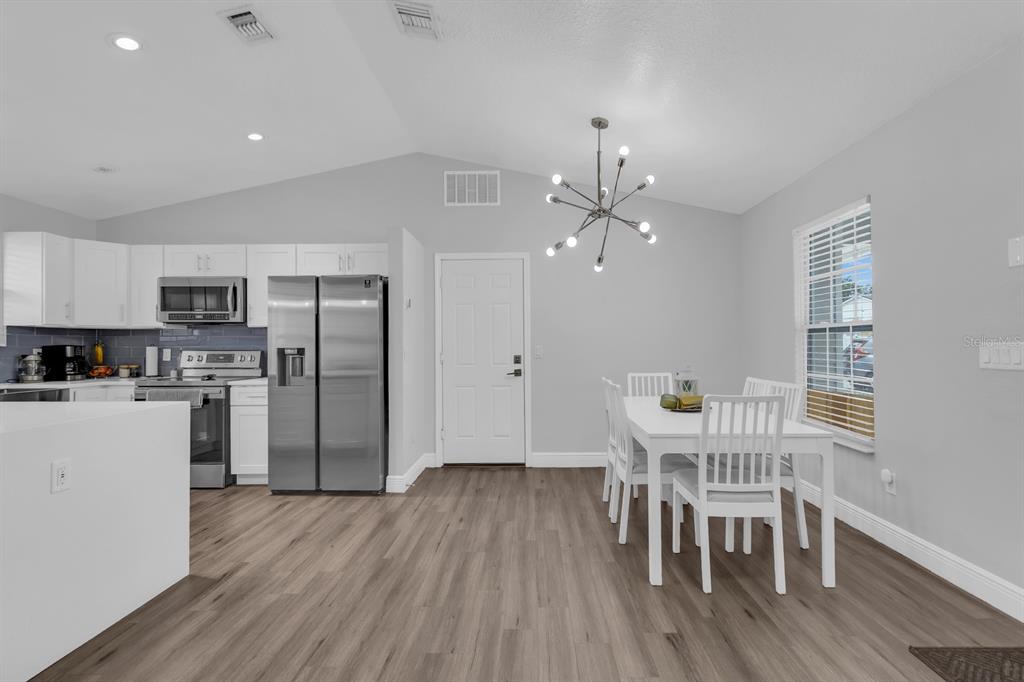 A dining area with a white table and chairs sits next to a modern kitchen — 8115 WINDY HILL WAY, ORLANDO, FL