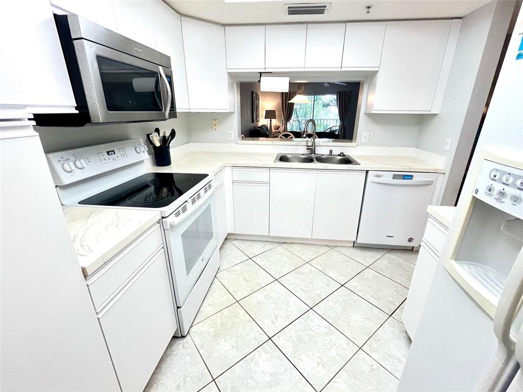 A white kitchen features tile flooring, stainless steel appliances, and a pass-through window — 6507 STONE RIVER ROAD UNIT 210, BRADENTON, FL