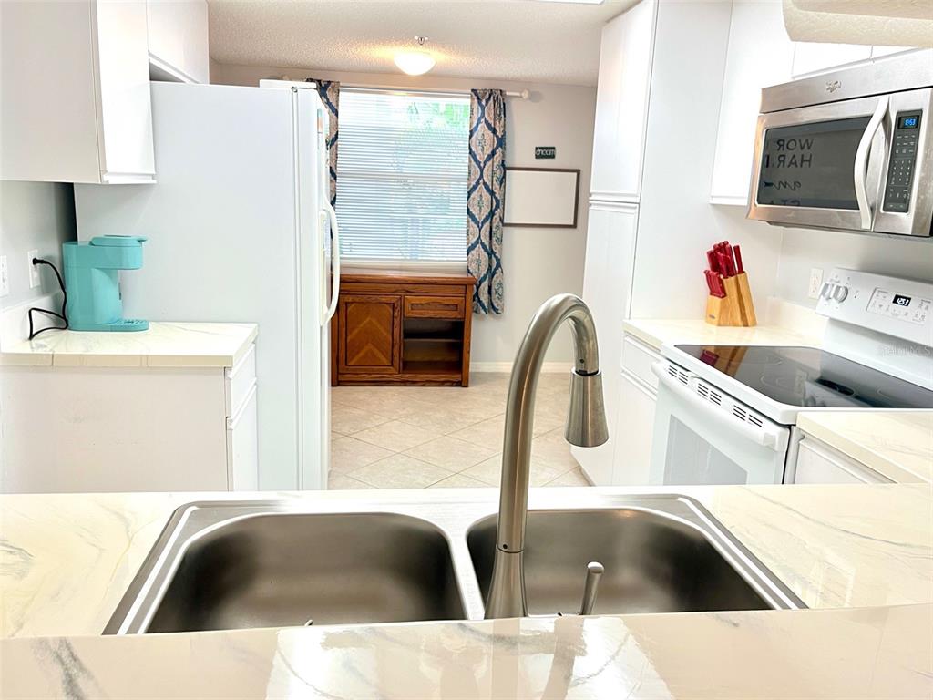 A kitchen features white cabinets, stainless steel appliances, a double sink, and a dining area — 6507 STONE RIVER ROAD UNIT 210, BRADENTON, FL