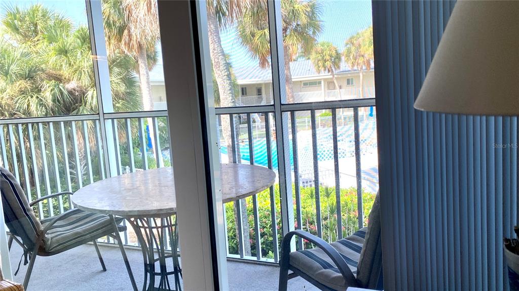 A screened-in balcony features a round table and two chairs overlooking a swimming pool — 500 S WASHINGTON DRIVE UNIT 24B, SARASOTA, FL