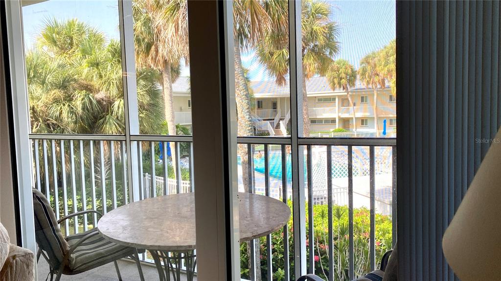 A screened-in balcony features a round table, chairs, and a view of a swimming pool — 500 S WASHINGTON DRIVE UNIT 24B, SARASOTA, FL