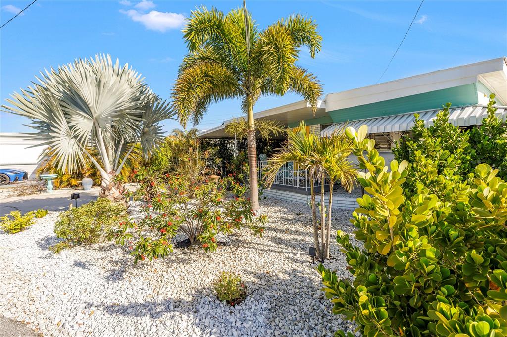 The exterior of a home features a white rock yard, palm trees, and a covered porch — 1703 MINNESOTA AVENUE, BRADENTON, FL