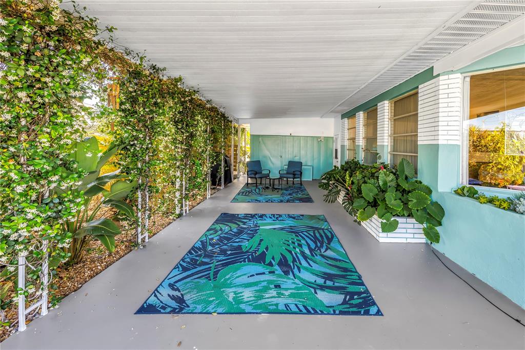 A covered patio features a gray floor, two area rugs, and a wall covered in vines — 1703 MINNESOTA AVENUE, BRADENTON, FL