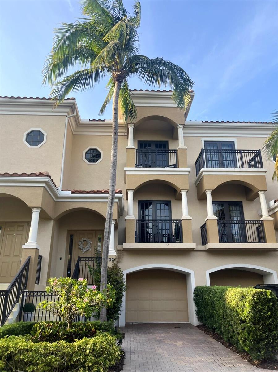 A three-story tan stucco townhouse features balconies, arched entryways, a garage, and a palm tree — 502 Del Sol Circle, Tequesta FL 33469, TEQUESTA, FL