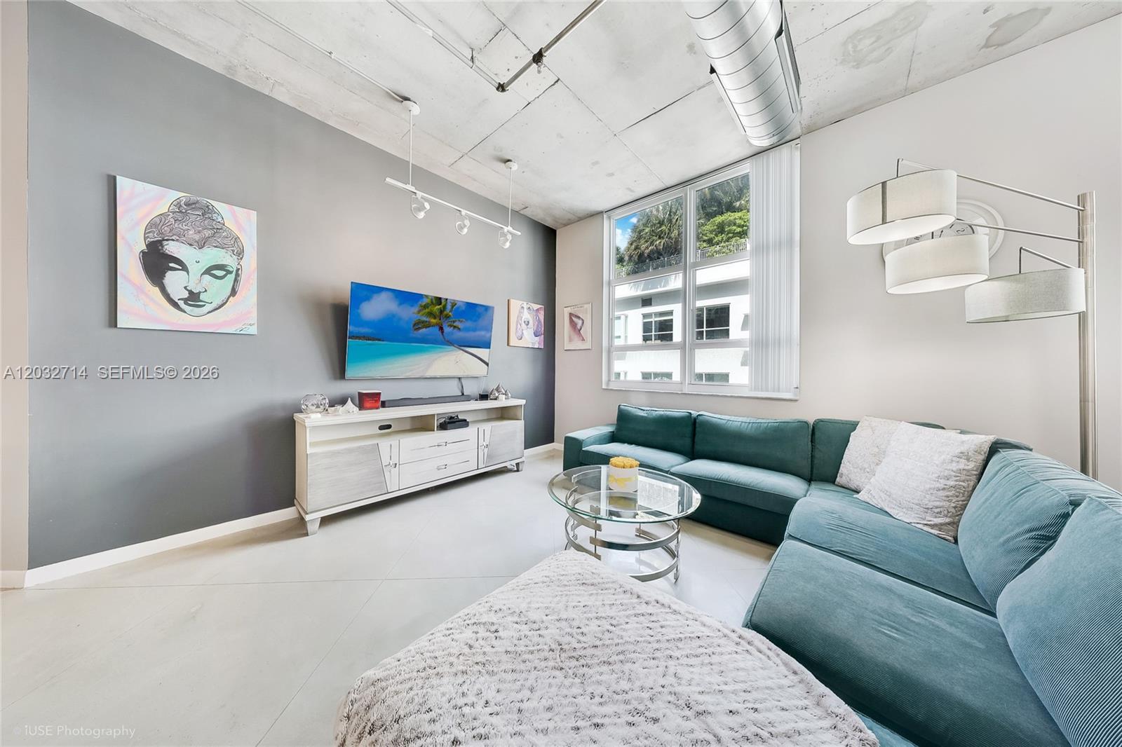 A living room features a teal sectional sofa, a gray accent wall, and exposed concrete ceilings — 2001 Biscayne Blvd # 2311, Miami FL 33137, MIAMI, FL