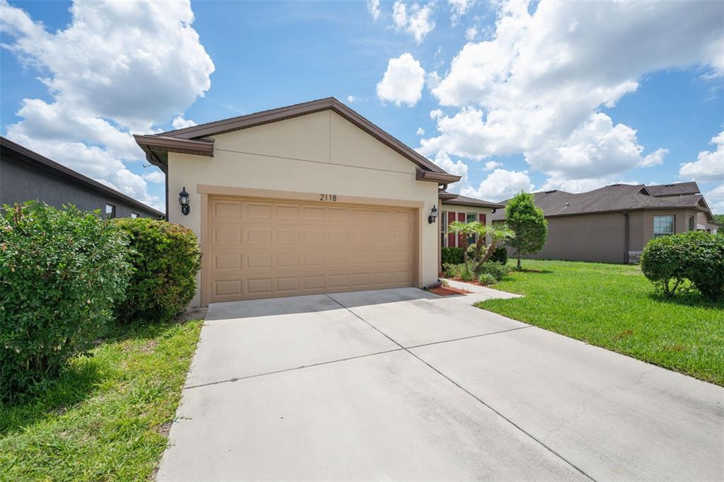 A beige single-story house features a two-car garage, a concrete driveway, and green landscaping — 2118 TRILLIUM BOULEVARD, BROOKSVILLE, FL