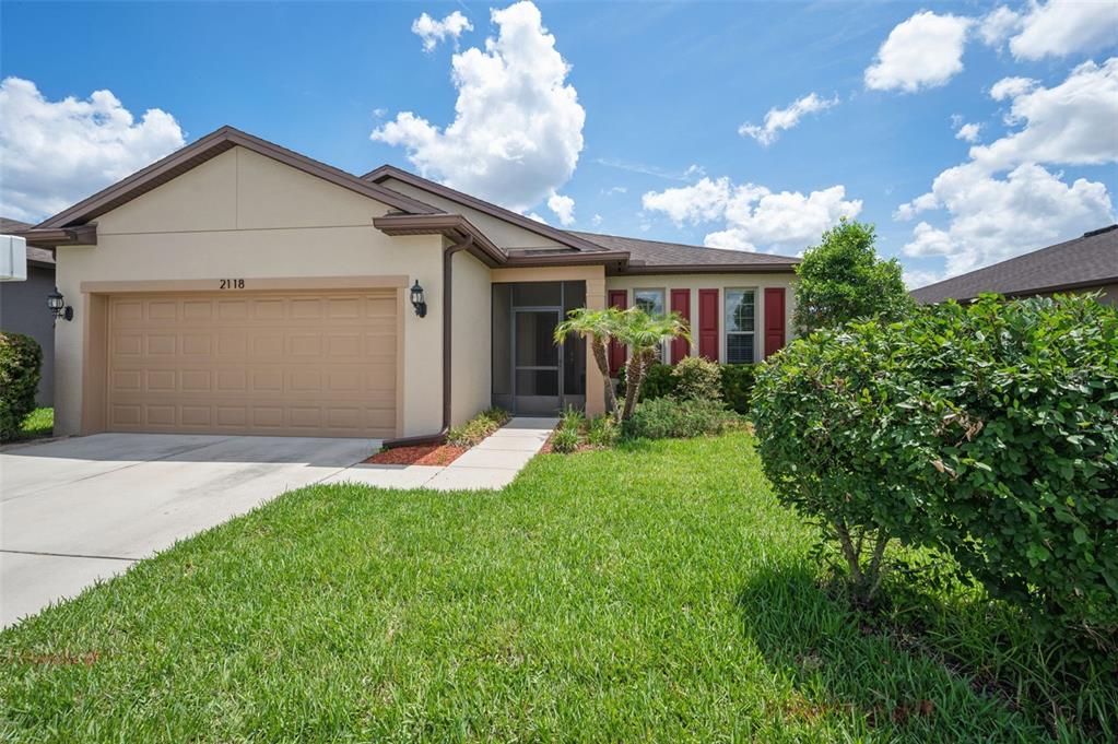 A single-story house with a tan stucco exterior, a two-car garage, and red shutters — 2118 TRILLIUM BOULEVARD, BROOKSVILLE, FL