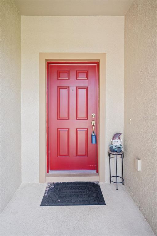 A red front door with a lockbox sits in a beige entryway with a welcome mat — 2118 TRILLIUM BOULEVARD, BROOKSVILLE, FL