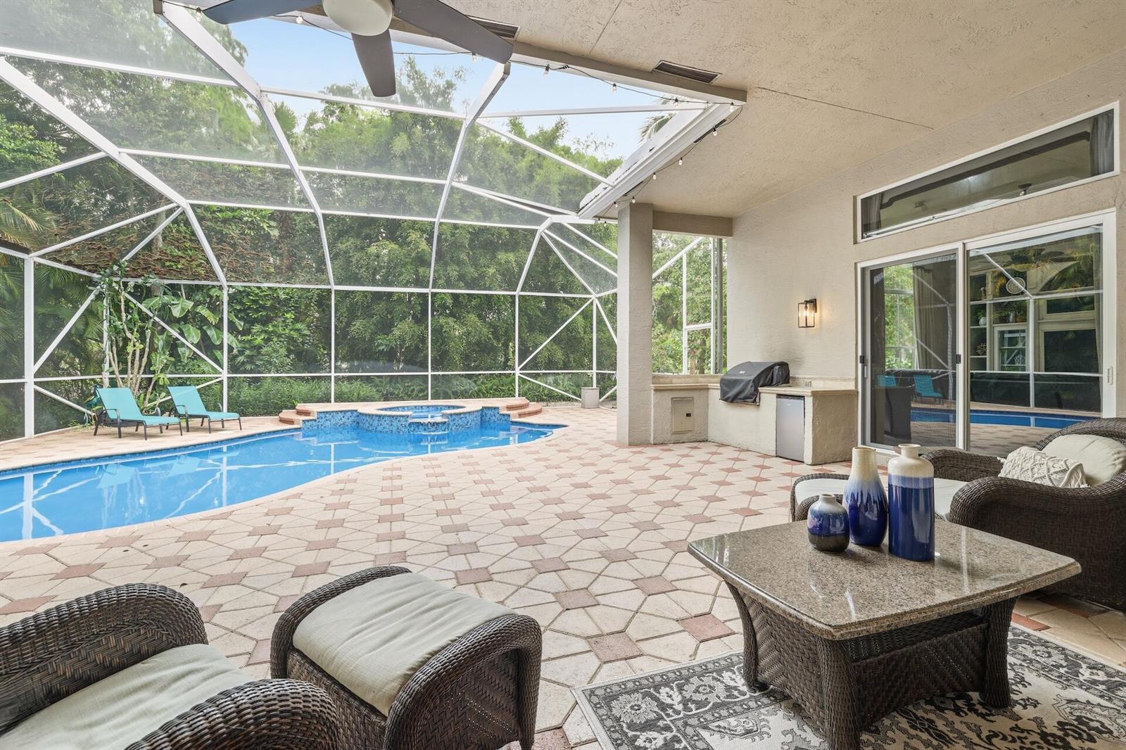 A covered patio features a swimming pool, hot tub, outdoor kitchen, and wicker furniture — 856 Forest Glen Lane, Wellington FL 33414, WELLINGTON, FL