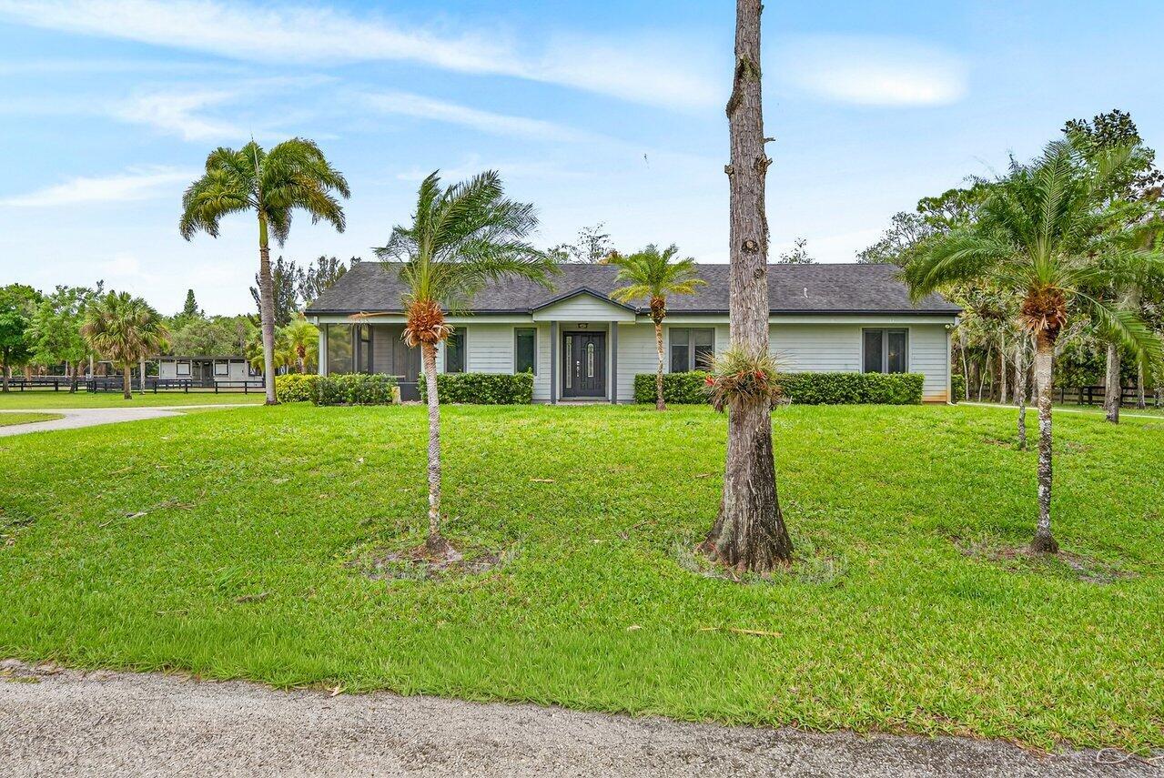 A single-story house with light-colored siding and a dark roof sits on a grassy lawn — 2741 Buck Ridge Trail, Loxahatchee FL 33470, LOXAHATCHEE, FL