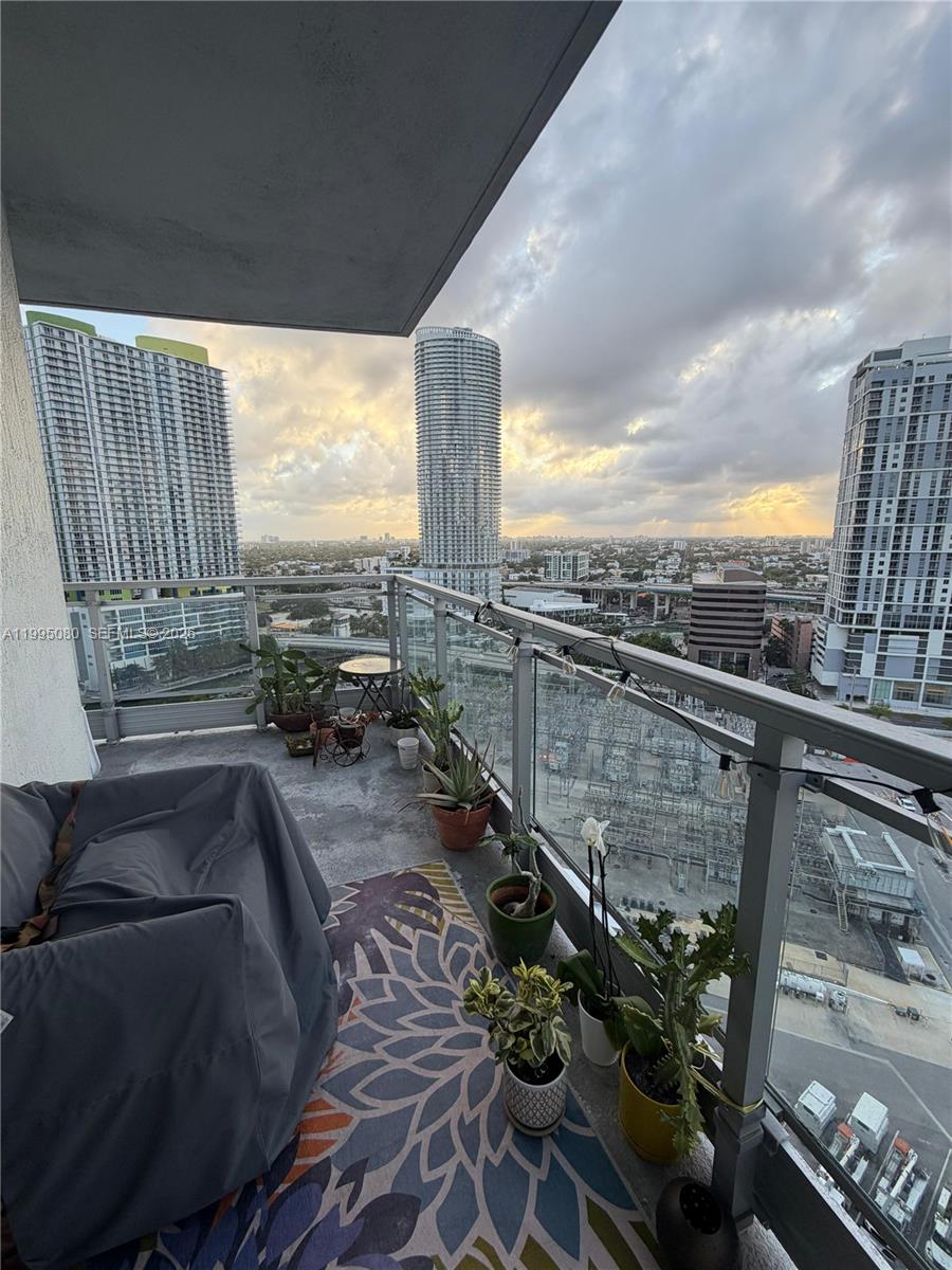 A balcony with potted plants, a covered chair, and a patterned rug overlooks city buildings — 90 SW 3RD STREET # 2112, Miami FL 33130, MIAMI, FL
